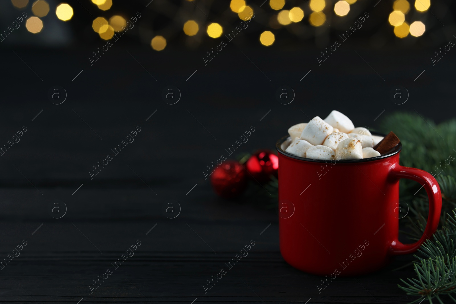 Photo of Tasty hot cocoa drink with marshmallows in mug and fir branches on black wooden table, closeup. Space for text