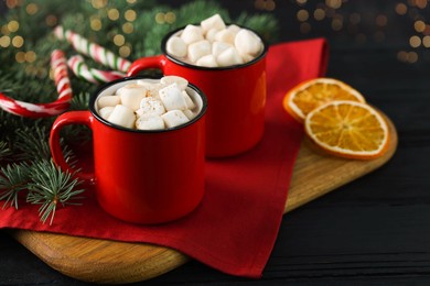 Photo of Tasty hot cocoa drinks with marshmallows in mugs and Christmas decor on black wooden table, closeup