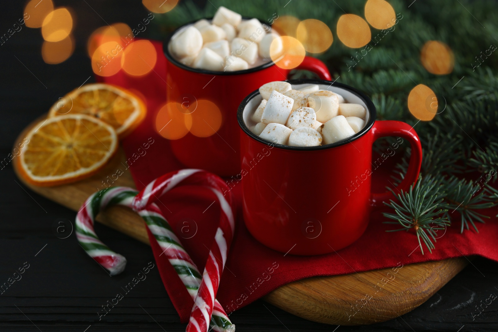 Photo of Tasty hot cocoa drinks with marshmallows in mugs and Christmas decor on black wooden table, closeup