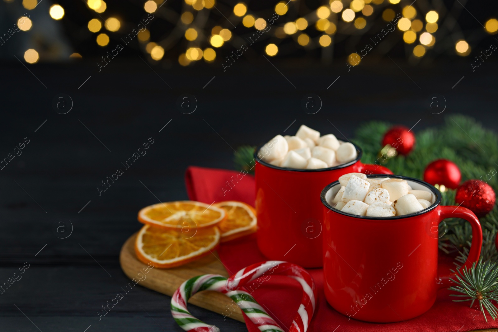 Photo of Tasty hot cocoa drinks with marshmallows in cups on black wooden table, closeup. Space for text