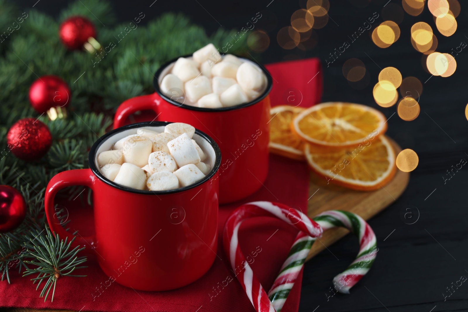 Photo of Tasty hot cocoa drinks with marshmallows in mugs and Christmas decor on black wooden table, closeup