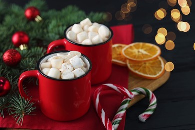 Photo of Tasty hot cocoa drinks with marshmallows in mugs and Christmas decor on black wooden table, closeup