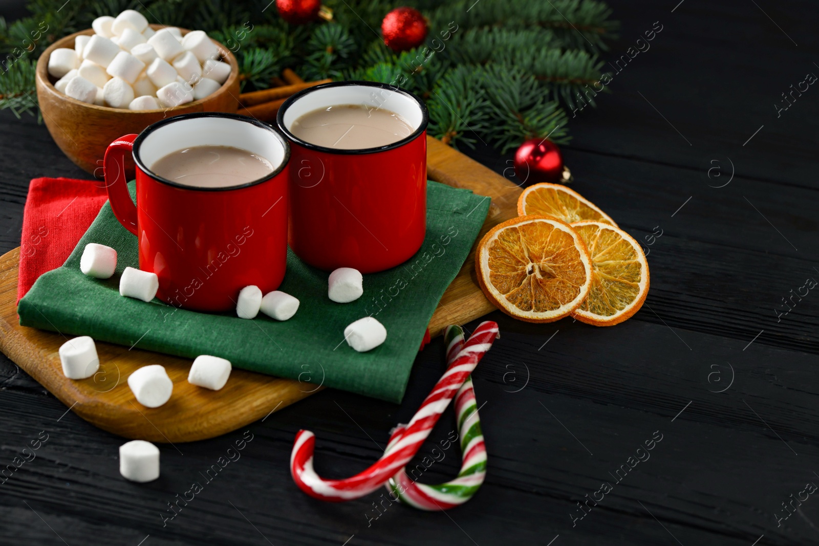 Photo of Tasty hot cocoa drinks in mugs, marshmallows and candy canes on black wooden table