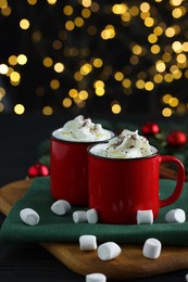 Photo of Tasty hot cocoa drinks with whipped cream in mugs and marshmallows on black wooden table, closeup