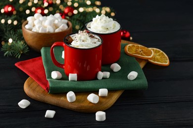 Photo of Tasty hot cocoa drinks with whipped cream in mugs and marshmallows on black wooden table, closeup