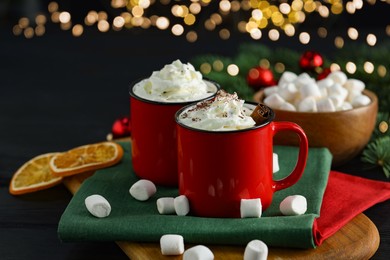 Photo of Tasty hot cocoa drinks with whipped cream in mugs and marshmallows on black table, closeup