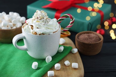 Photo of Tasty hot cocoa drink with whipped cream in cup and marshmallows on black wooden table, closeup