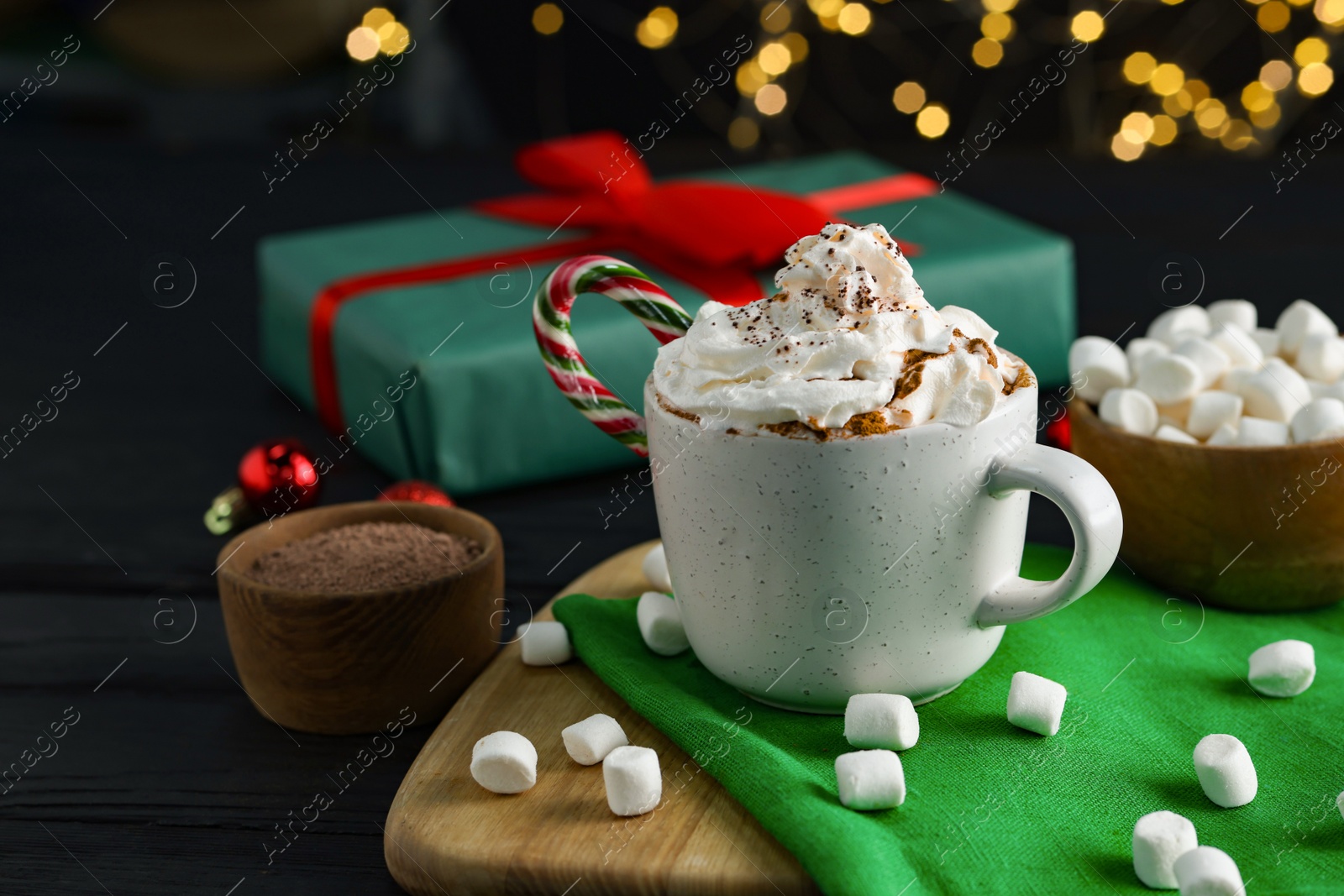 Photo of Tasty hot cocoa drink with whipped cream in cup and marshmallows on black wooden table, closeup