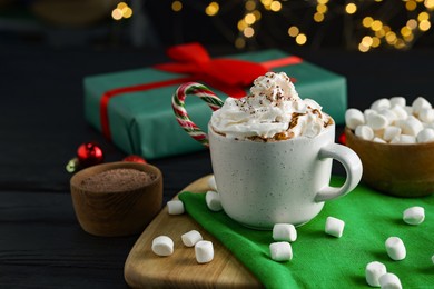 Photo of Tasty hot cocoa drink with whipped cream in cup and marshmallows on black wooden table, closeup