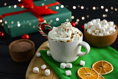 Photo of Tasty hot cocoa drink with whipped cream in cup and marshmallows on black wooden table, closeup