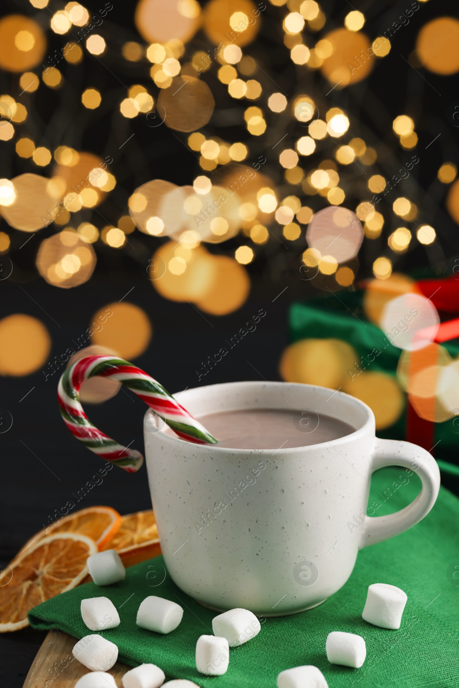 Photo of Tasty hot cocoa drink with candy cane in cup and marshmallows on table, closeup