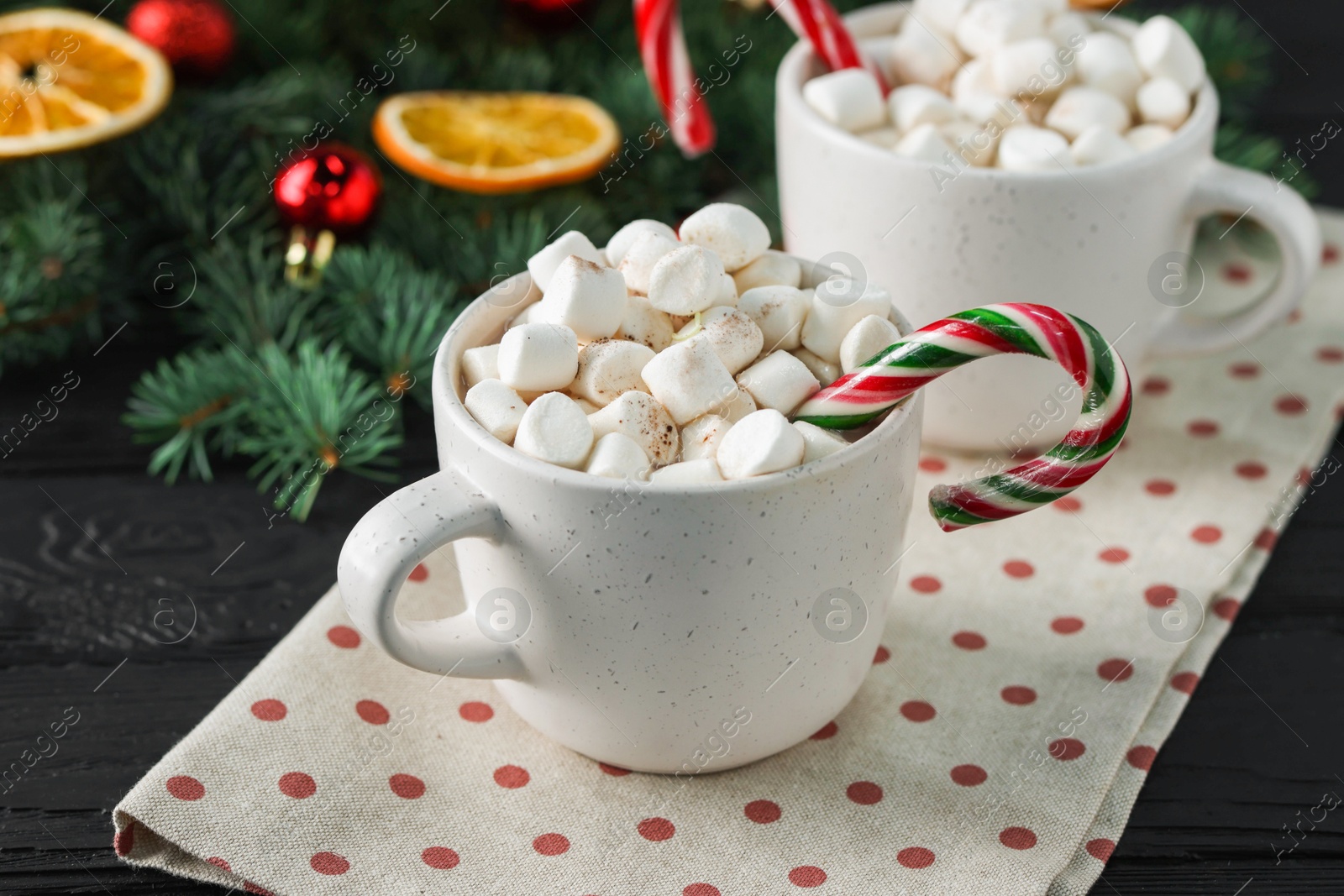 Photo of Tasty hot cocoa drinks with candy canes and marshmallows in cups on black wooden table, closeup