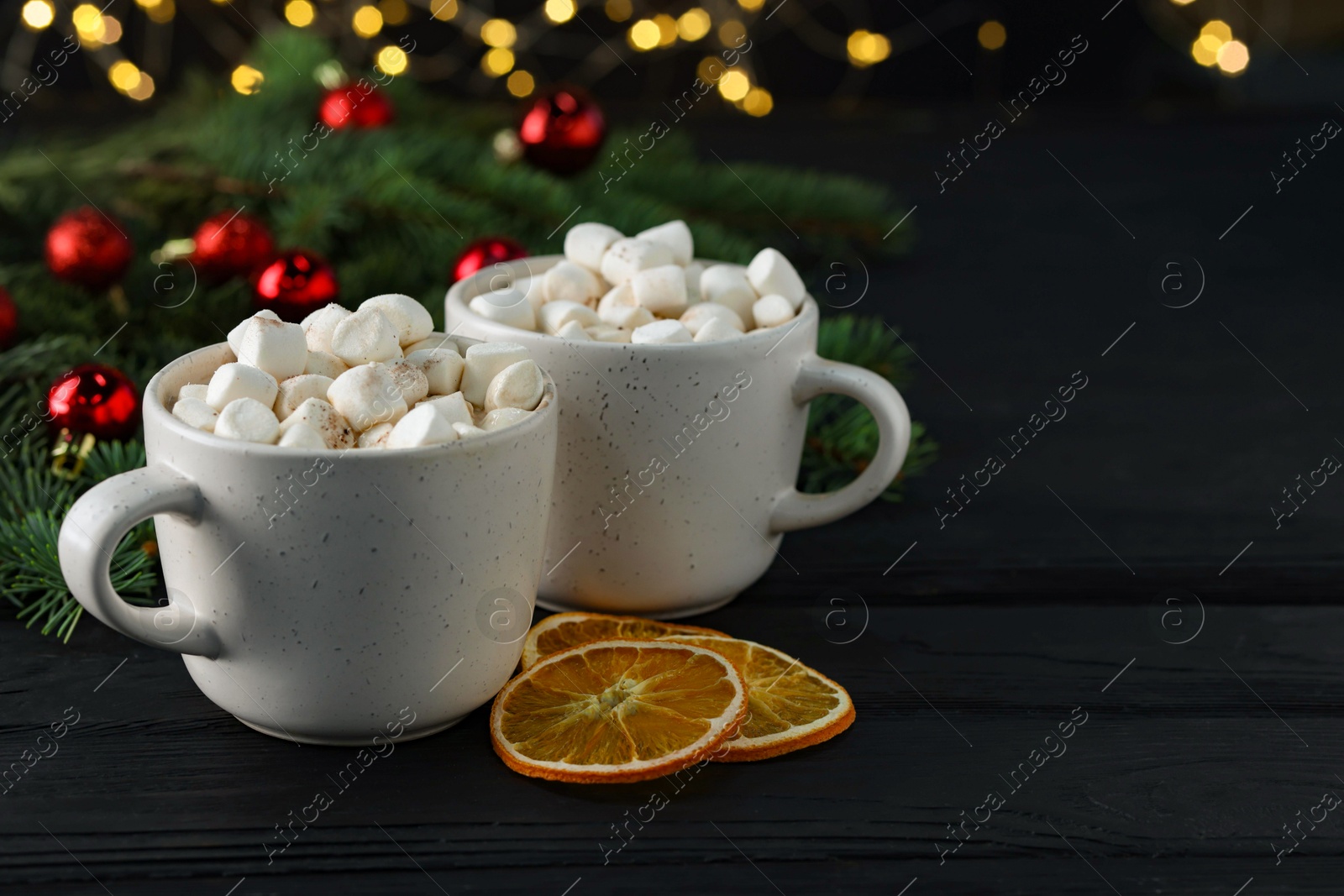 Photo of Tasty hot cocoa drinks with marshmallows in cups and dry orange slices on black wooden table, closeup. Space for text