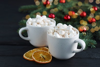 Photo of Tasty hot cocoa drinks with marshmallows in cups and dry orange slices on black wooden table, closeup