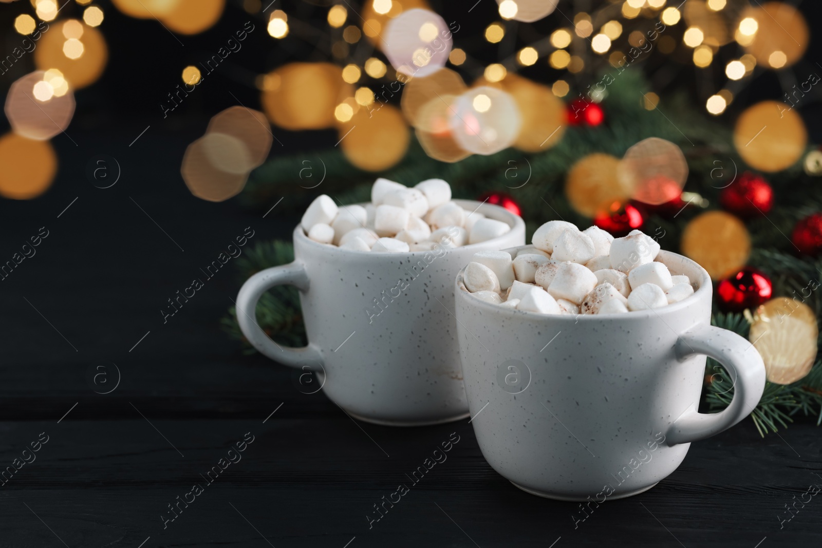 Photo of Tasty hot cocoa drinks with marshmallows in cups on black wooden table, closeup. Space for text