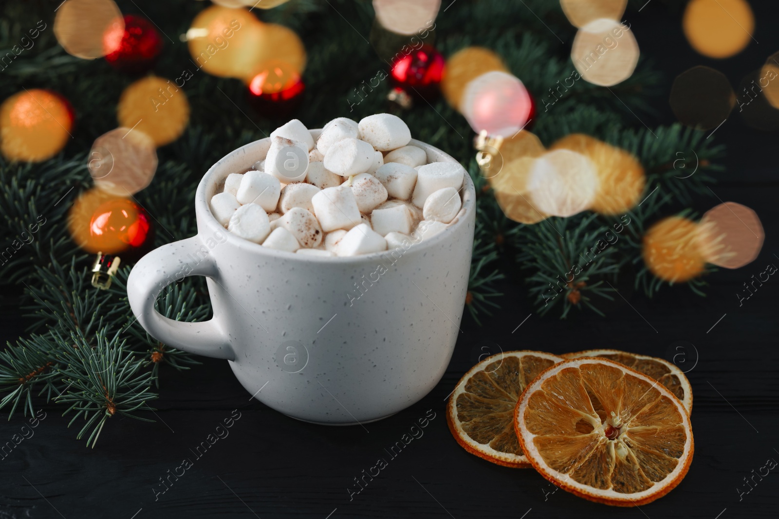 Photo of Tasty hot cocoa drink with marshmallows in cup and dry orange slices on black table, closeup