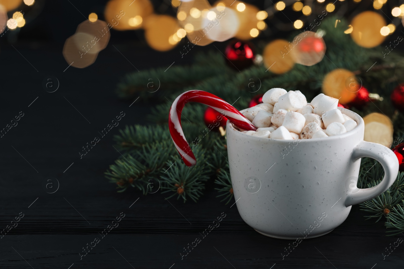 Photo of Tasty hot cocoa drink with candy cane, marshmallows in cup and Christmas decor on black wooden table, closeup. Space for text