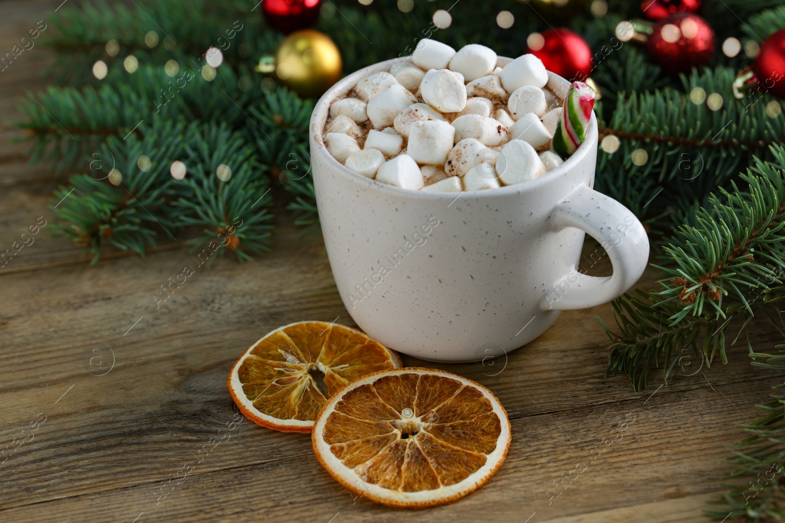 Photo of Tasty hot cocoa drink with candy cane, marshmallows in cup and dry orange slices on wooden table, closeup