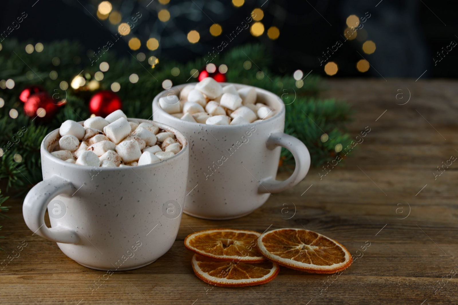 Photo of Tasty hot cocoa drinks with marshmallows in cups and dry orange slices on wooden table, closeup