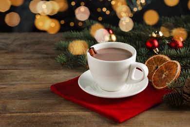 Photo of Tasty hot cocoa drink with cinnamon sticks in cup and dry orange slices on wooden table, closeup. Space for text