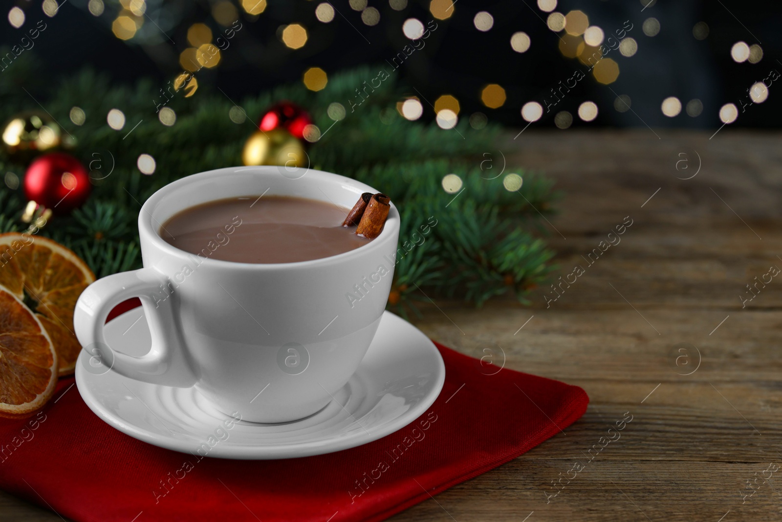 Photo of Tasty hot cocoa drink with cinnamon sticks in cup and dry orange slices on wooden table, closeup. Space for text