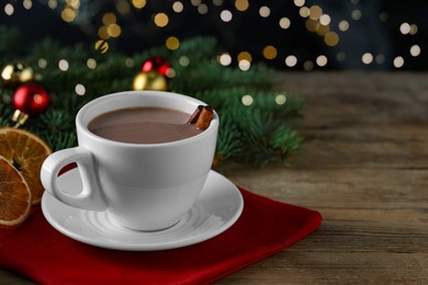 Photo of Tasty hot cocoa drink with cinnamon sticks in cup and dry orange slices on wooden table, closeup. Space for text