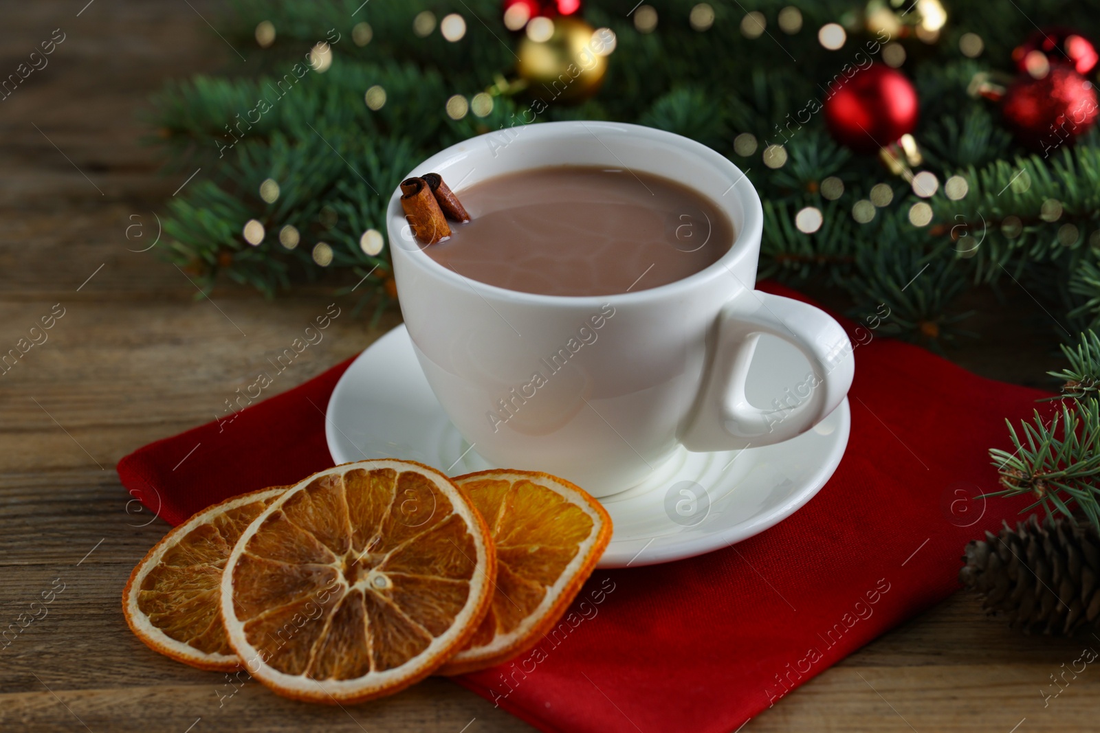 Photo of Tasty hot cocoa drink with cinnamon sticks in cup and dry orange slices on wooden table, closeup