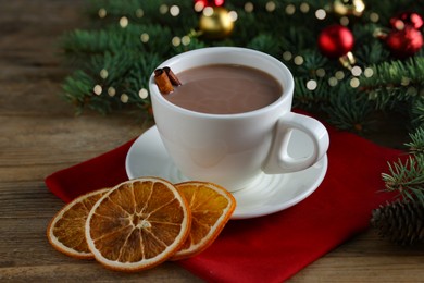 Photo of Tasty hot cocoa drink with cinnamon sticks in cup and dry orange slices on wooden table, closeup