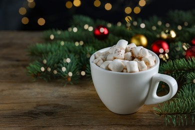 Photo of Tasty hot cocoa drink with marshmallows, cinnamon stick in cup and fir branches on wooden table, closeup. Space for text