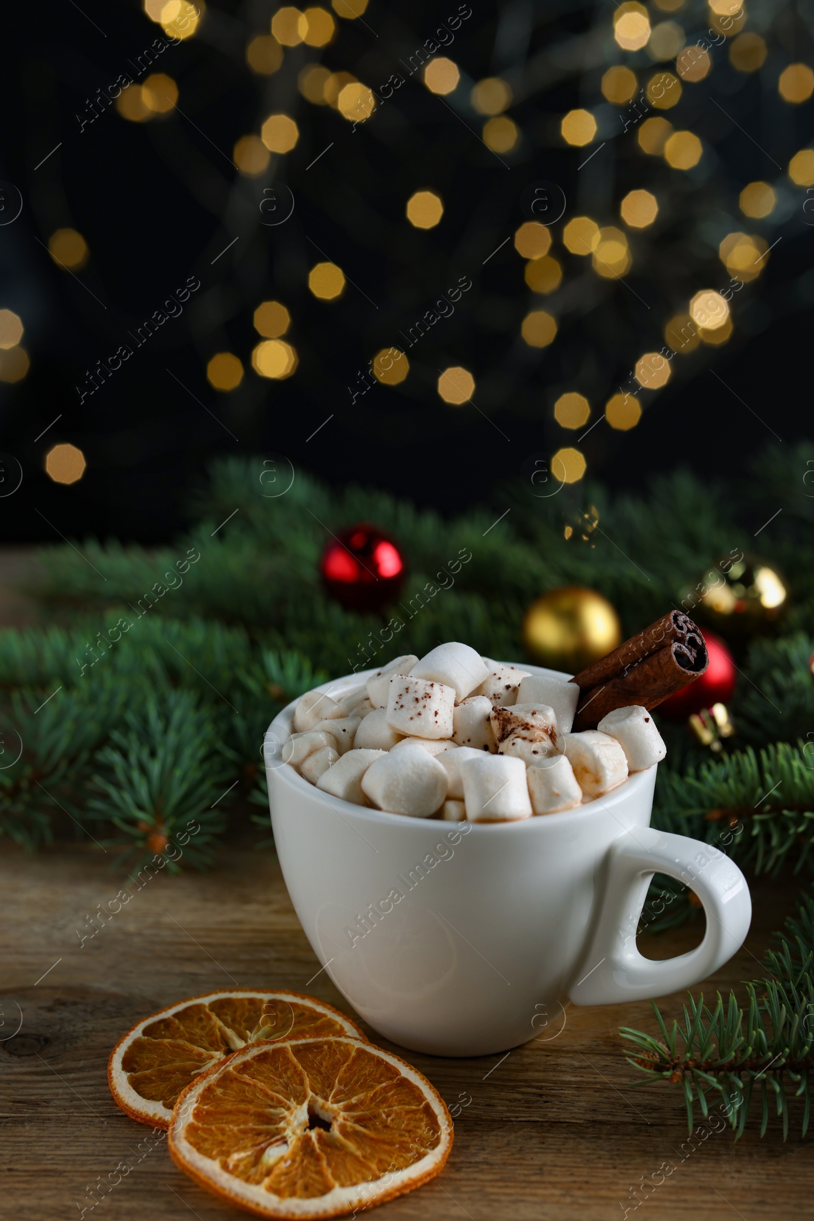 Photo of Tasty hot cocoa drink with marshmallows, cinnamon stick in cup and dry orange slices on wooden table, closeup