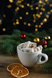 Photo of Tasty hot cocoa drink with marshmallows, cinnamon stick in cup and dry orange slices on wooden table, closeup