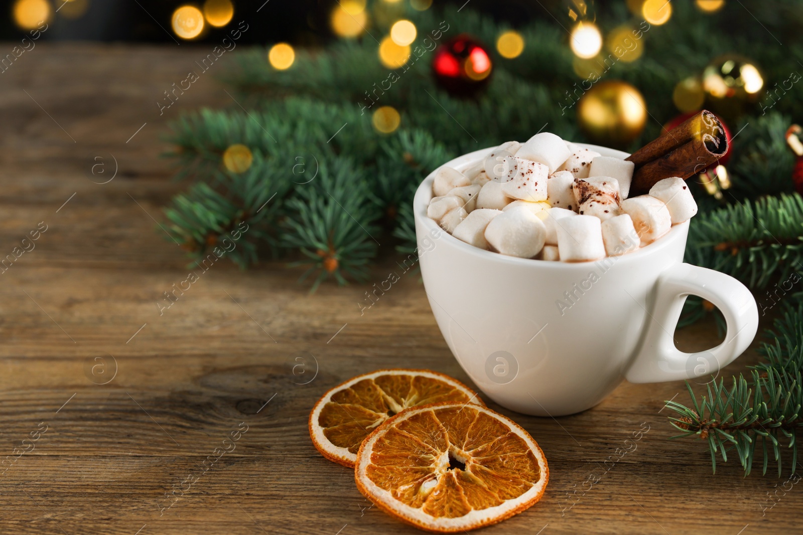 Photo of Tasty hot cocoa drink with marshmallows, cinnamon stick in cup and dry orange slices on wooden table, closeup. Space for text