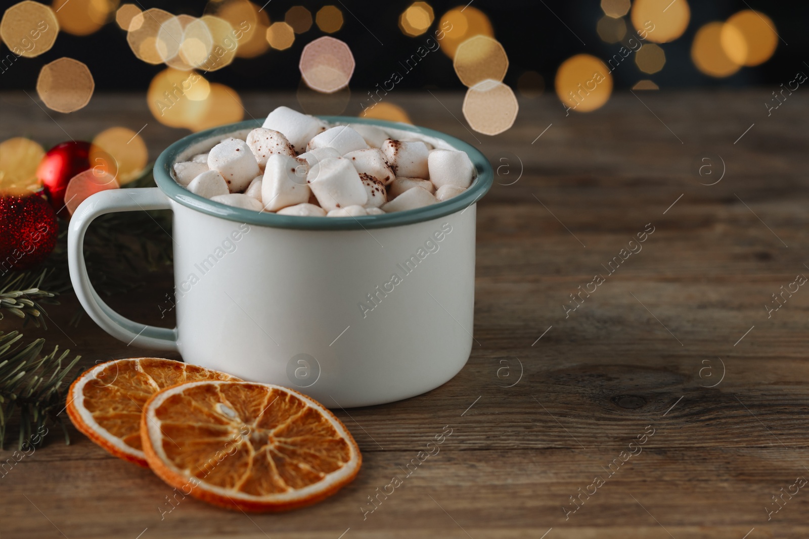 Photo of Tasty hot cocoa drink with marshmallows in cup and dry orange slices on wooden table, closeup. Space for text