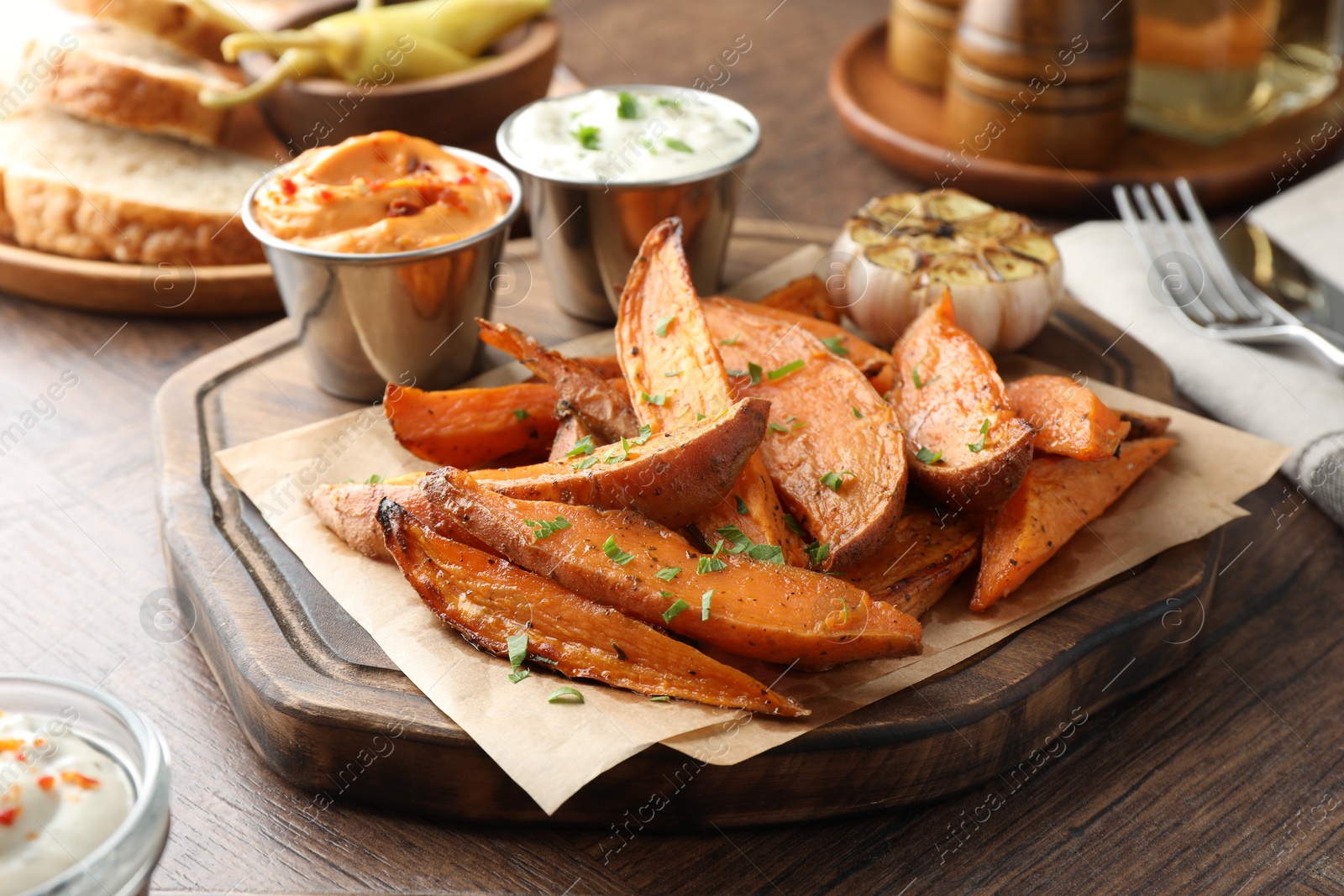 Photo of Tasty cooked sweet potatoes served with sauces on wooden table, closeup