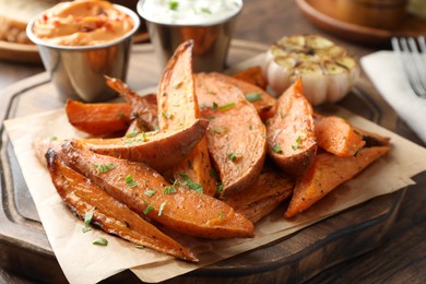 Photo of Tasty cooked sweet potatoes served with sauces on wooden table, closeup