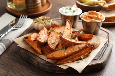 Photo of Tasty cooked sweet potatoes served with sauces on wooden table, closeup