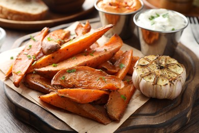 Photo of Tasty cooked sweet potatoes served with sauces on table, closeup