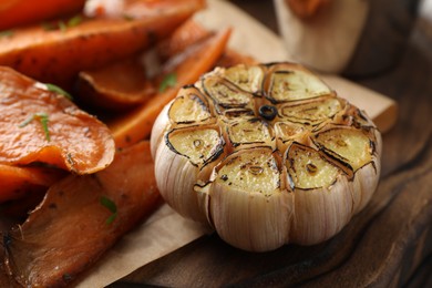 Photo of Tasty cooked sweet potatoes and garlic on table, closeup