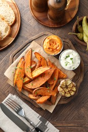 Photo of Tasty cooked sweet potatoes served with sauces on wooden table, top view