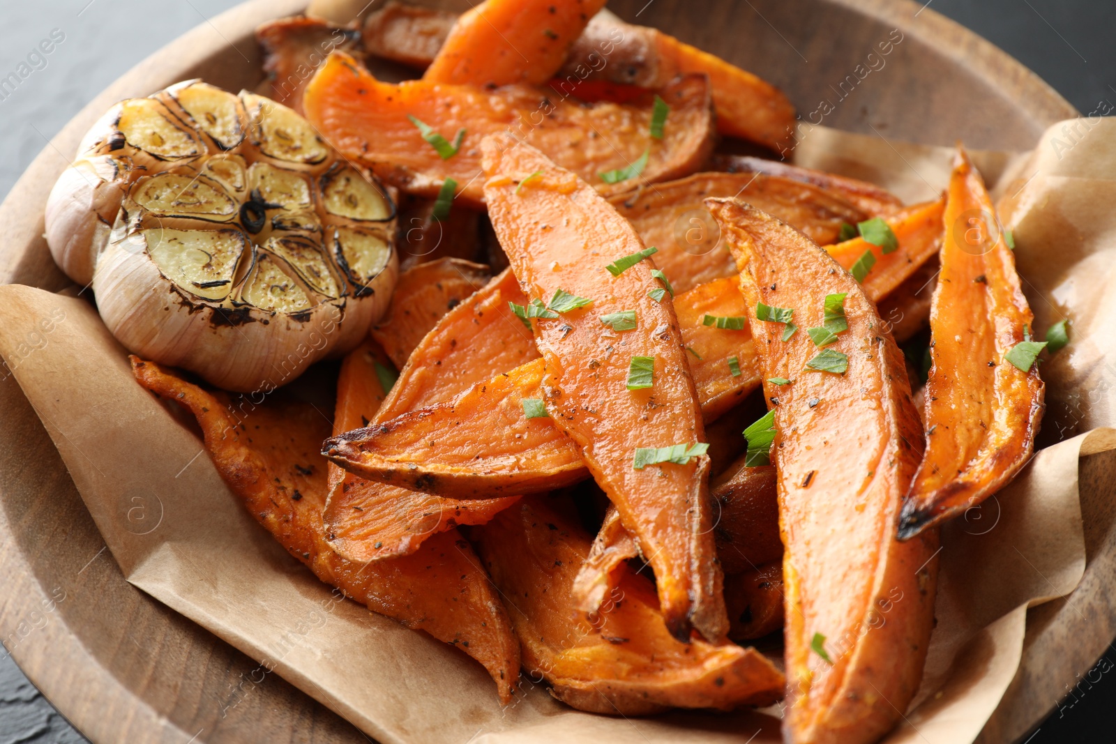 Photo of Tasty cooked sweet potatoes with parsley and garlic on table, closeup