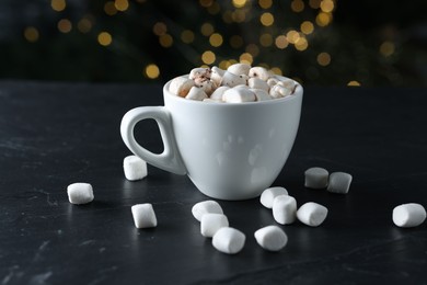 Photo of Tasty hot cocoa drink with marshmallows in cup on black textured table