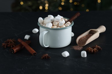 Photo of Tasty hot cocoa drink with marshmallows in mug and spices on black table