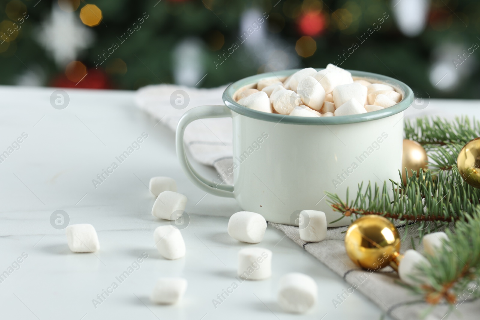 Photo of Tasty hot cocoa drink with marshmallows in mug and Christmas decor on white table against blurred lights, closeup. Space for text