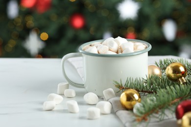 Photo of Tasty hot cocoa drink with marshmallows in mug and Christmas decor on white table against blurred lights, closeup. Space for text