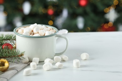 Photo of Tasty hot cocoa drink with marshmallows in mug and Christmas decor on white table against blurred lights, closeup. Space for text