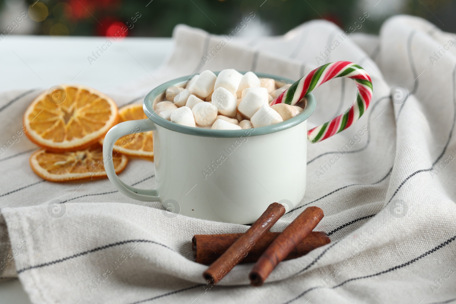 Photo of Tasty hot cocoa drink with marshmallows, candy cane in mug and spices on table, closeup