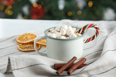 Photo of Tasty hot cocoa drink with marshmallows, candy cane in mug and spices on table, closeup