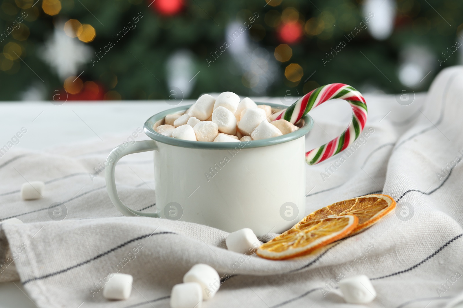 Photo of Tasty hot cocoa drink with marshmallows, candy cane in mug and dry orange slices on table, closeup