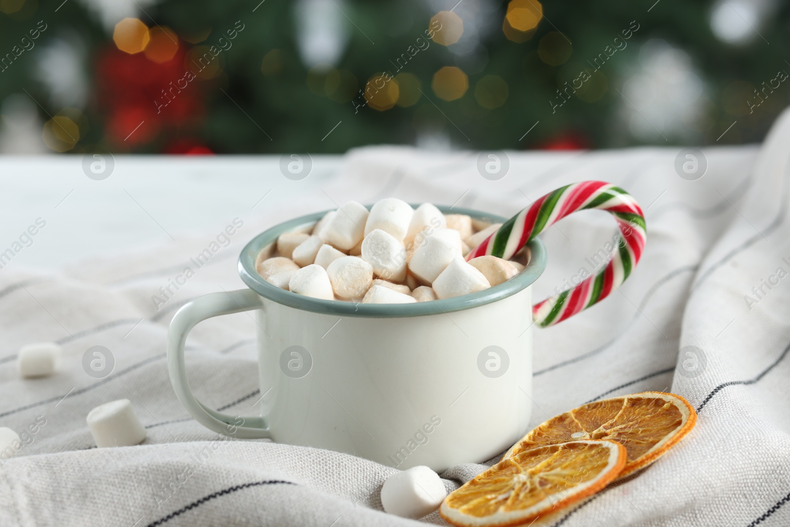 Photo of Tasty hot cocoa drink with marshmallows, candy cane in mug and dry orange slices on table, closeup