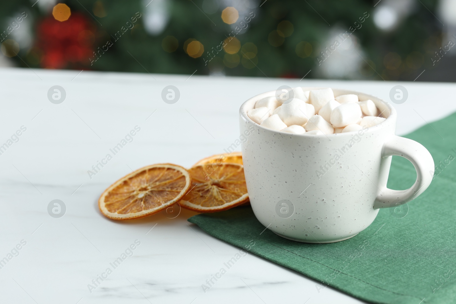 Photo of Tasty hot cocoa drink with marshmallows in cup and dry orange slices on white table, closeup. Space for text